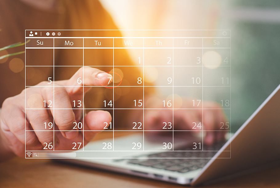 There is a floating hologram of a calendar beside a laptop. A person's finger is interacting with the calendar.