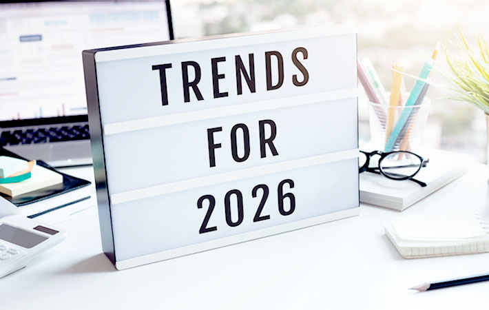 A sign sits on a desk, reading "Trends for 2026," eluding to eye care trends. Behind the sign, folded eye glasses, stationery, and a laptop depicting data and graphs.
